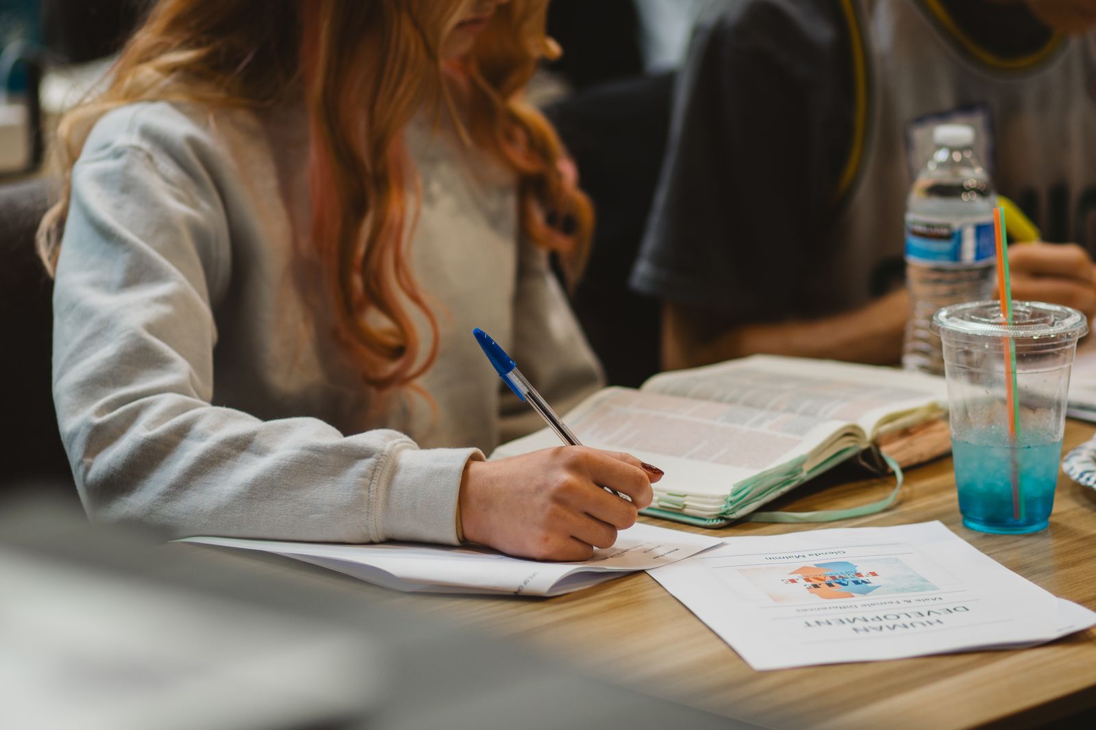 Student taking notes beside an open Bible in class